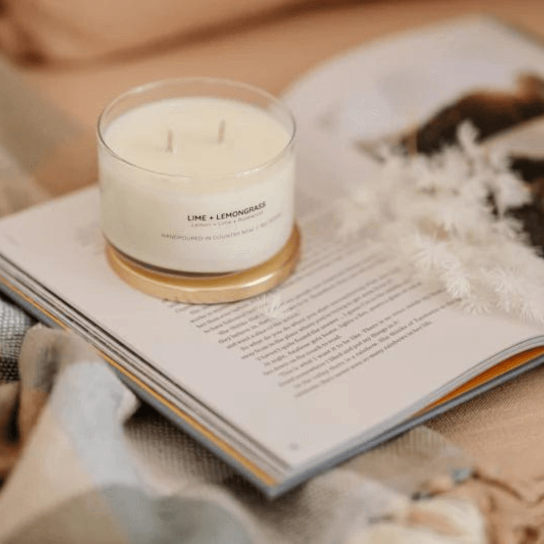 Candle labeled 'Lime + Lemongrass' on an open book with a soft background
