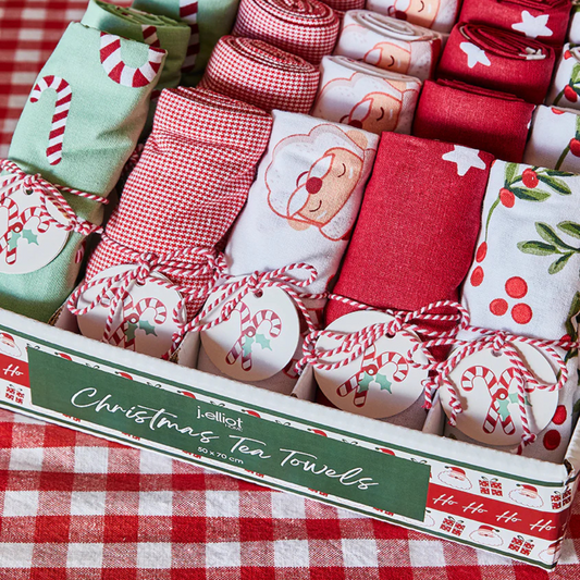 Collection of Christmas-themed tea towels in a box on a red checkered tablecloth.