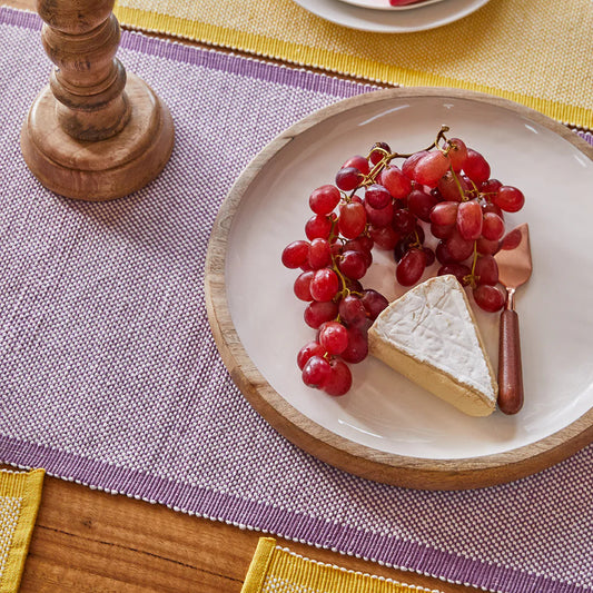 Plated cheese and grapes on a wooden table with a pink napkin.