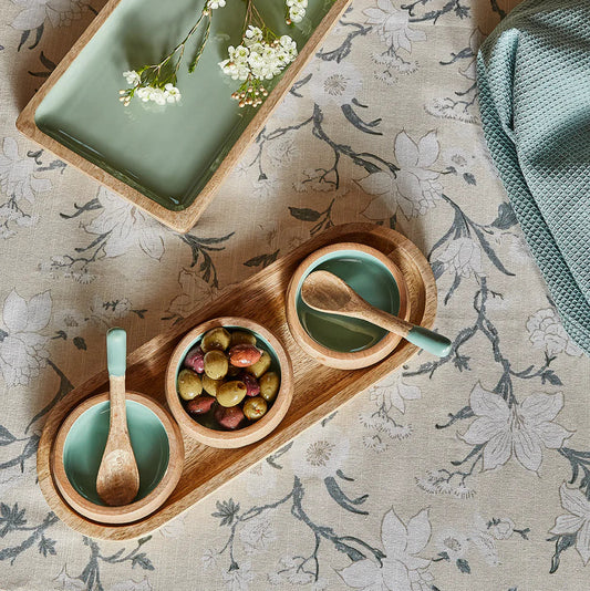 Wooden tray with ceramic bowls and spoons on a floral-patterned surface
