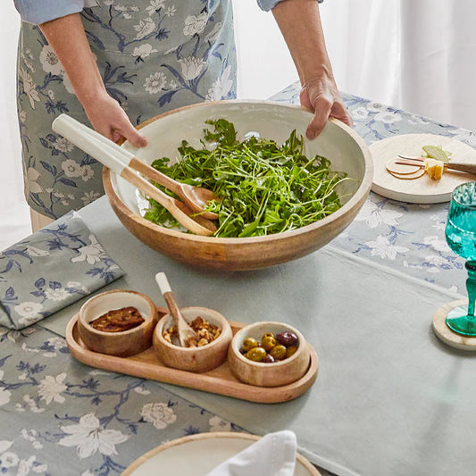 Person holding a large bowl of salad on a table with a floral tablecloth.