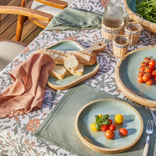 Outdoor dining setup with plates of food, glasses, and a bottle on a patterned tablecloth.