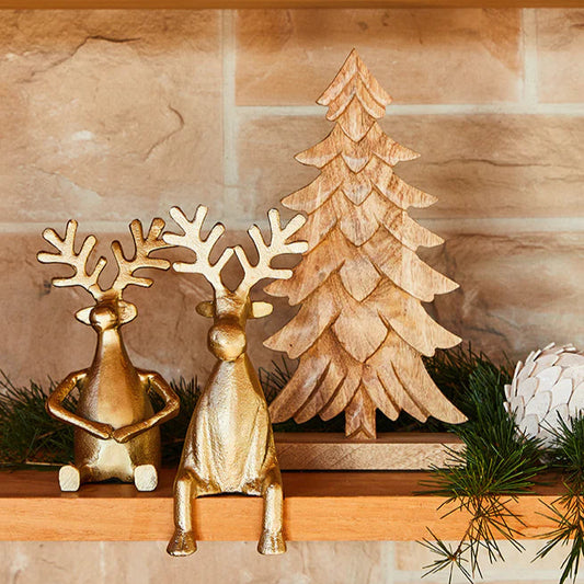 Decorative mantel with gold deer, tree, and white ball against a stone wall.